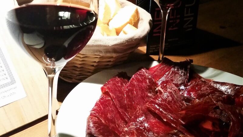 glass of red wine with dried ham next to it